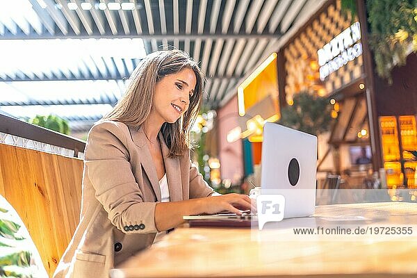 Seitenansicht einer fröhlichen eleganten Geschäftsfrau mit Laptop in einer Cafeteria