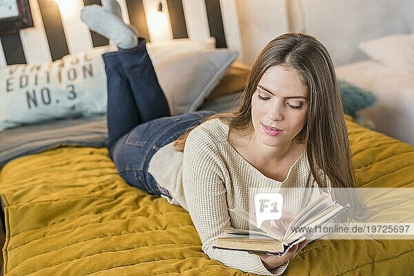 Attraktive junge Frau genießt das Lesen Buch Bett
