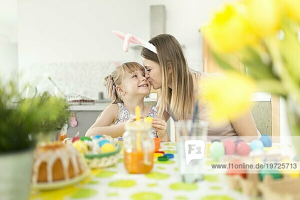 Frau küsst Tochter beim Verzieren von Ostereiern