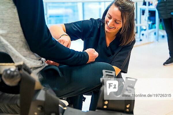 Mechanisches Exoskelett. Physiotherapie lächelnd in modernem Krankenhaus: Eine Physiotherapeutin hilft einer behinderten Person mit einem Roboterskelett mit Bändern. Futuristische Rehabilitation