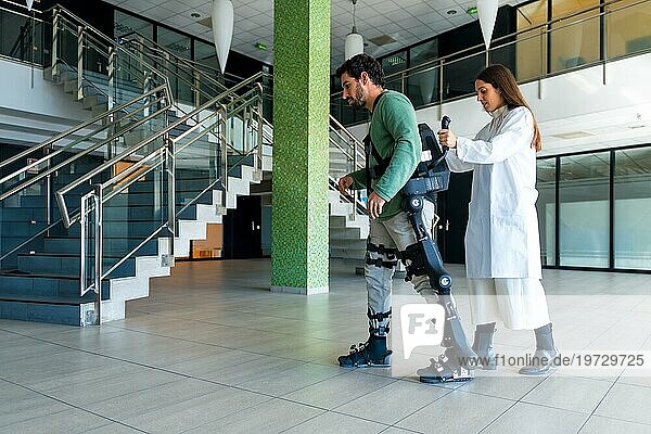 Mechanisches Exoskelett  Ärztin  Physiotherapeutin  die mit einer behinderten Person mit Hilfe eines Roboterskeletts geht  Physiotherapie in einem modernen Krankenhaus  futuristische Physiotherapie