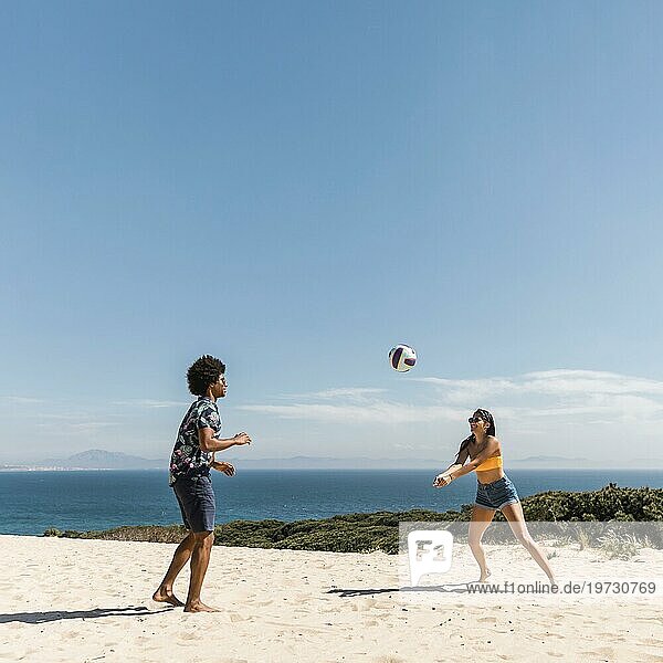Junges multikulturelles Paar spielt Volleyball am Strand