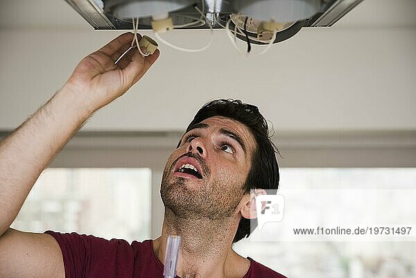 Nahaufnahme eines männlichen Elektrikers bei der Installation einer Halterung für eine Deckenleuchte