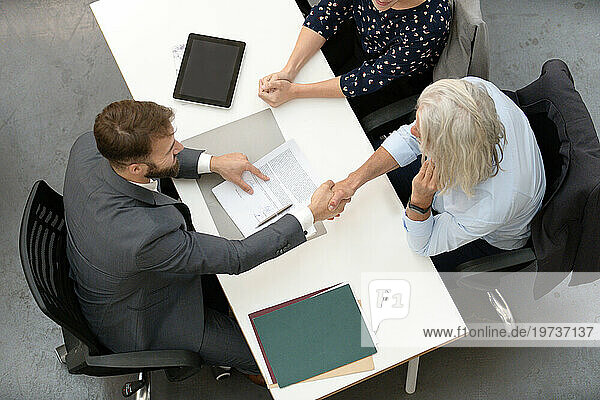 Adult couple shaking hands with lawyer after signing contract