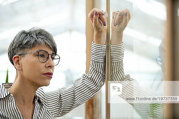 Thoughtful businesswoman leaning on glass door