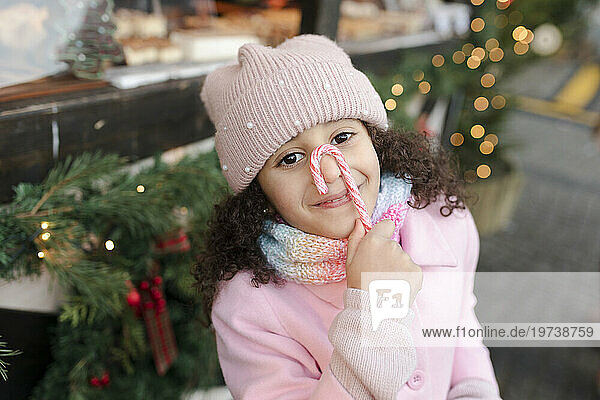 Smiling girl holding candy cane over face at Christmas market