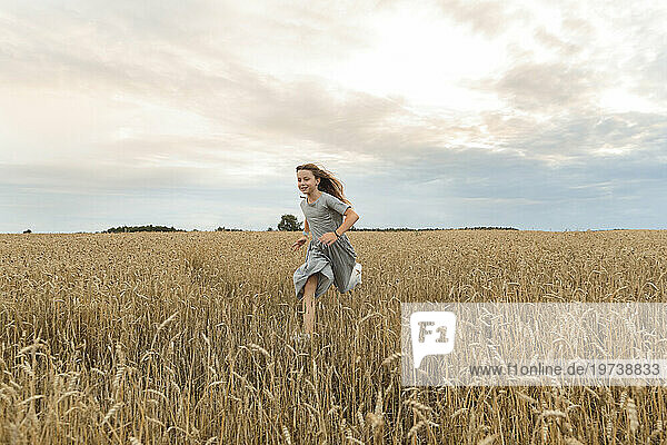 Happy girl running amidst field under sky