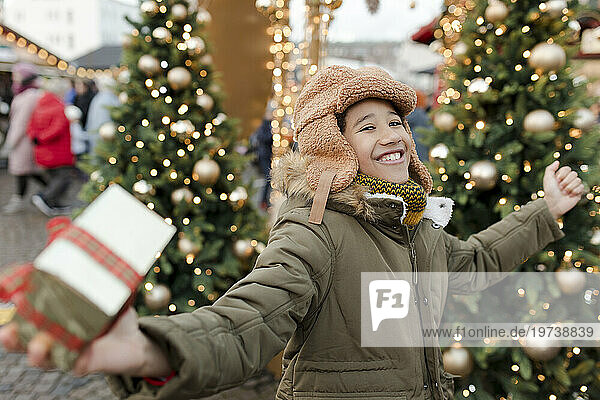 Cheerful boy holding gift box and enjoying at Christmas market