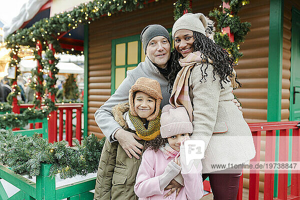 Happy family standing together in front of wooden house at Christmas market
