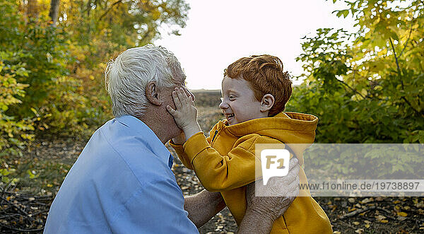 Cheerful boy embracing with grandfather in autumn forest