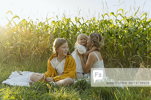 Girl with mother embracing and kissing daughter in field