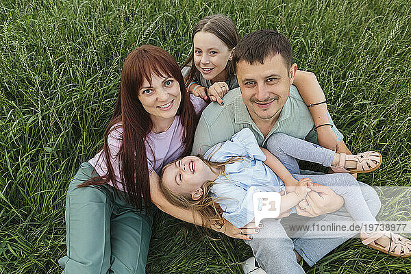 Happy parents with daughters sitting and having fun in field