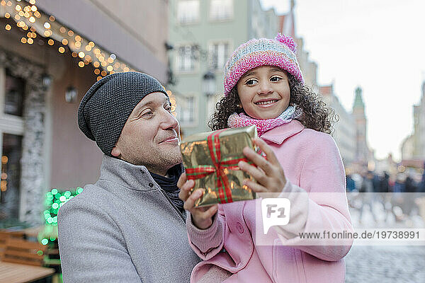 Smiling father with daughter holding gift at Christmas market