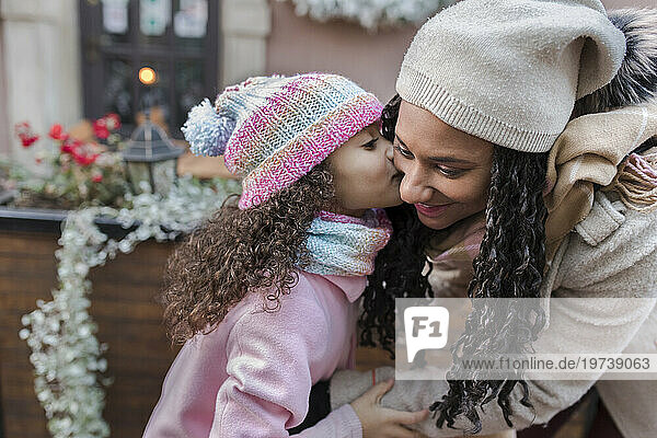 Girl kissing mother on cheeks at Christmas market