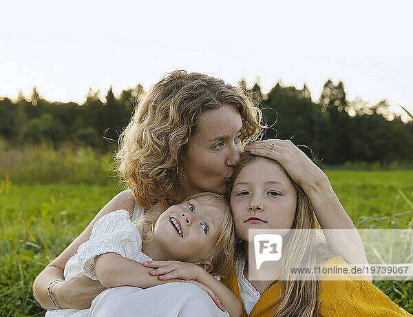 Mother kissing and embracing daughters in field