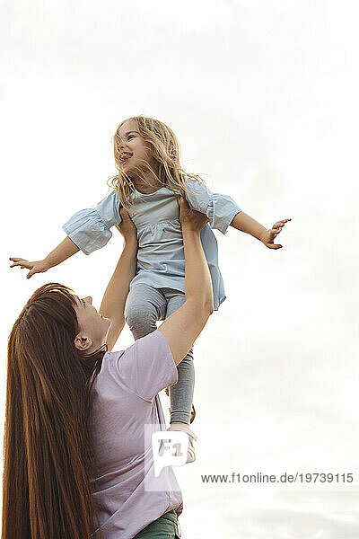 Happy mother lifting daughter under sky