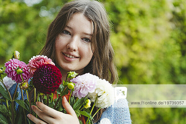 Smiling teenage girl holding dahlia flowers in front of plants