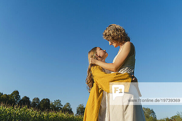 Smiling mother and daughter embracing each other under blue sky