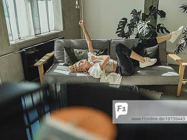 Carefree woman listening to music lying on sofa at home