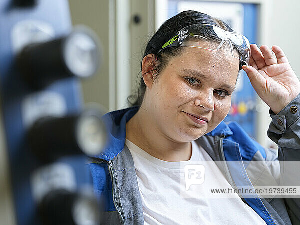 Smiling apprentice wearing protective eyeglasses at workshop