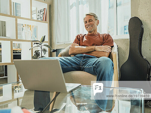 Smiling man with arms crossed watching laptop at home