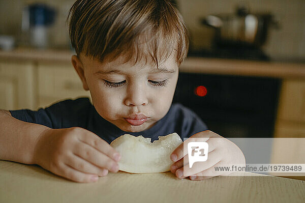 Boy eating slice of melon at table
