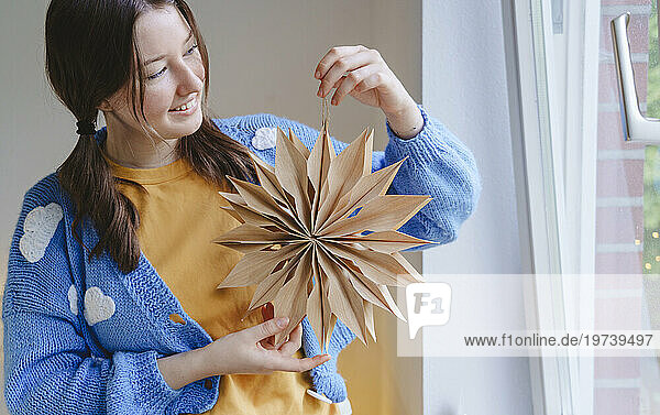 Smiling teenage girl holding star shaped Christmas decoration at home