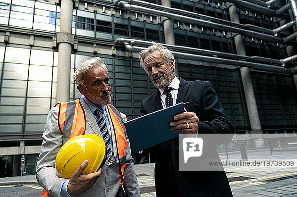 Smiling businessman discussing with colleague over tablet PC on road