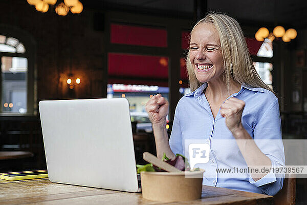 Smiling freelancer looking at laptop and cheering in pub