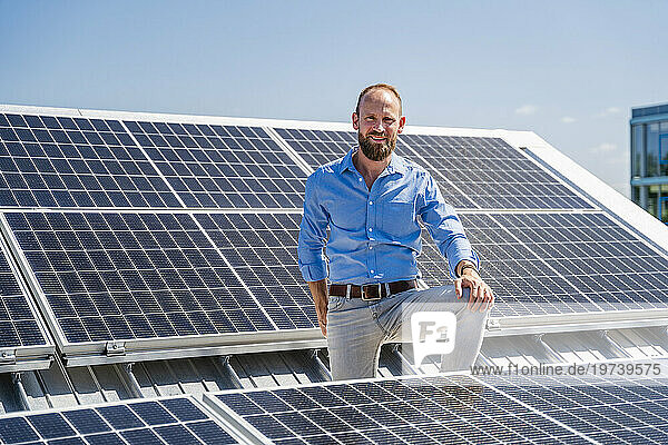 A cheerful businessman stands surrounded by solar panels  showcasing his commitment to sustainable energy
