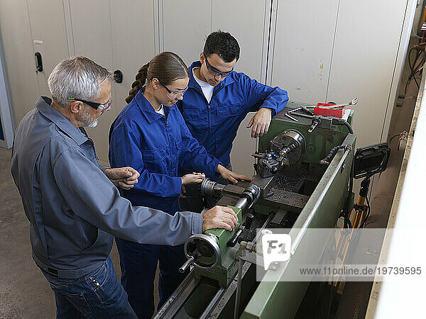 Instructor assisting trainees operating lathe at workshop