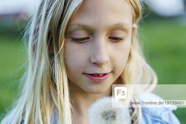Blond smiling girl looking at dandelion