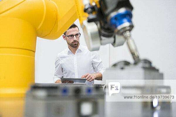 Engineer with tablet PC operating robotic arm in factory