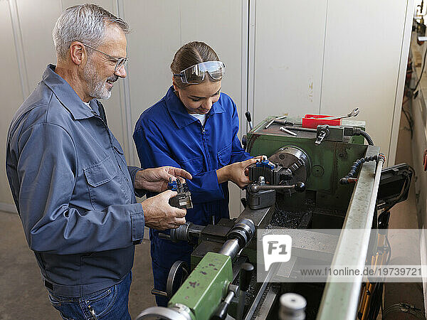 Trainee working with instructor standing near lathe machine at workshop