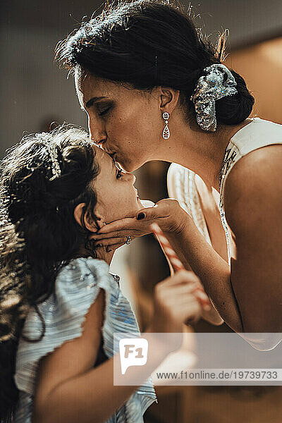 Mother kissing daughter on forehead at home
