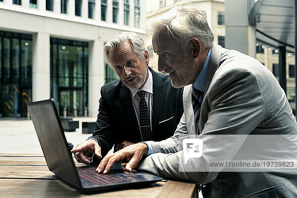 Senior businessman discussing with colleague over laptop at table