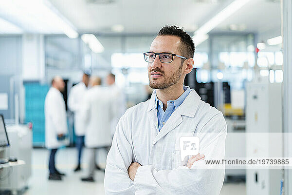 Confident electrical technician standing in electronics factory with arms crossed