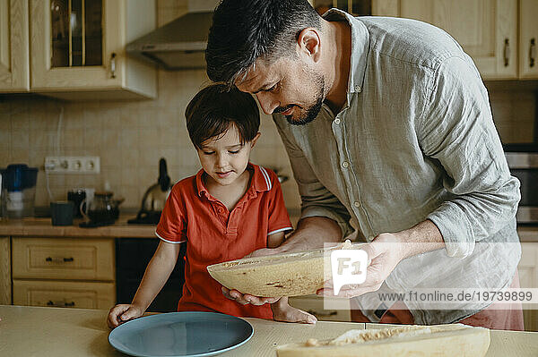 Father serving sliced melon to son in kitchen