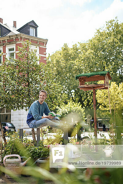 Smiling man holding book sitting in garden