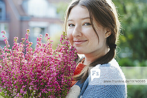 Smiling girl holding heather flowers on sunny day