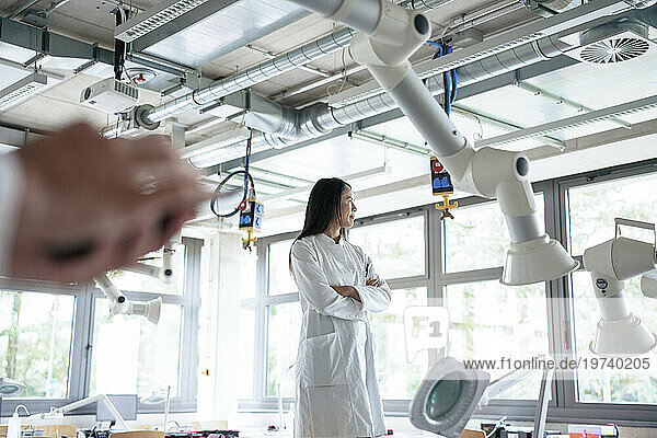 Thoughtful scientist standing near robotic arms in front of window at laboratory
