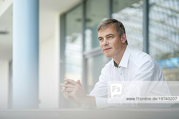 Serene businessman leaning on railing in office building