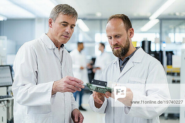 Colleagues in electronics factory discussing over motherboard