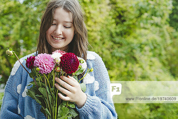 Happy girl holding dahlia flowers in front of plants