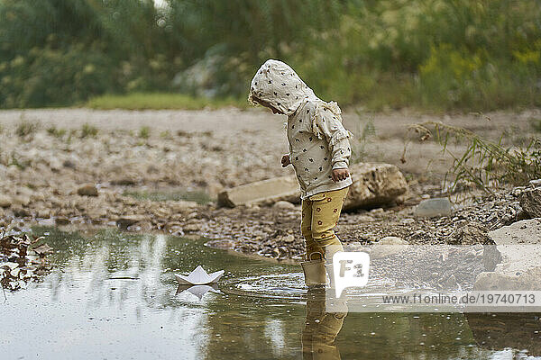 Girl with paper boat floating on water puddle
