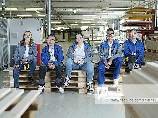 Smiling apprentices sitting on pallets at workshop
