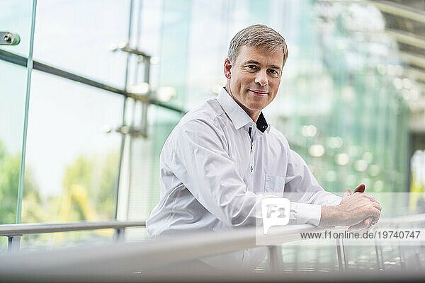 Confident businessman leaning on railing in office building
