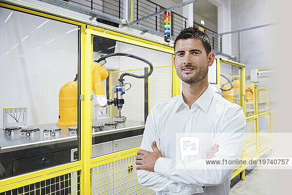 Smiling engineer with arms crossed standing at factory