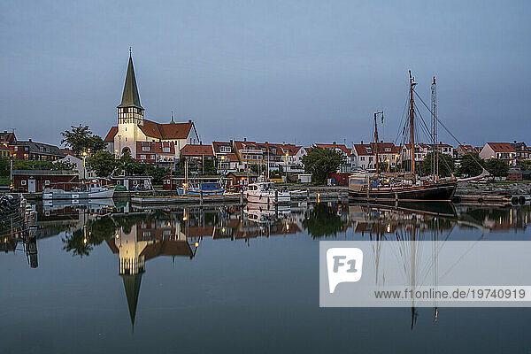 Denmark  Bornholm  Ronne  St Nicholas Church and surrounding houses reflecting in coastal water at dusk