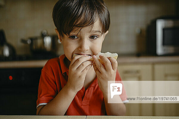 Boy wearing red shirt and eating melon at home
